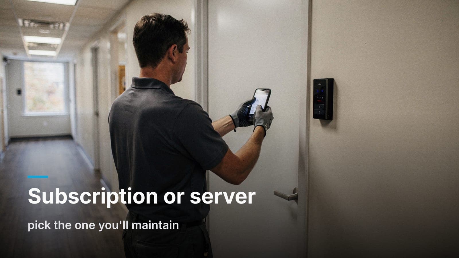 Person seen from behind holding a phone to a slim black card reader beside an office door in a sunlit hallway.