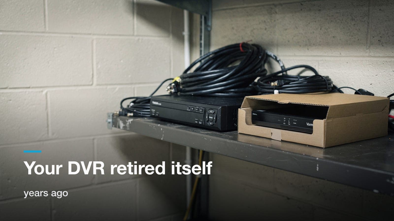 Old DVR with coils of black coax on a shelf beside a new network video recorder in its open box.