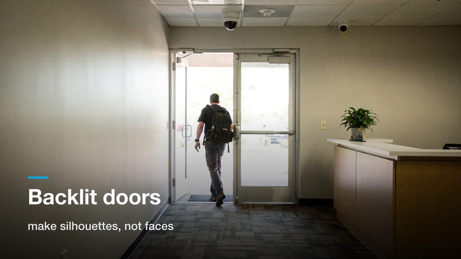 Person entering a sunlit glass office door as a backlit silhouette, with a ceiling dome camera aimed at the glare.