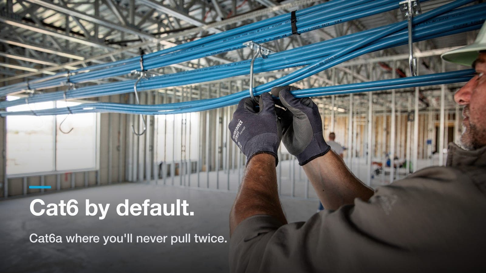 Two neatly dressed blue cable bundles, one thicker than the other, on J-hooks in an unfinished commercial ceiling.