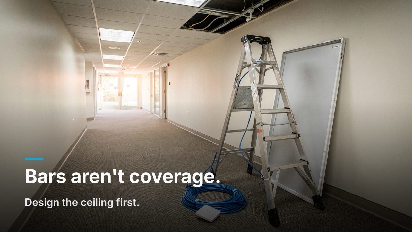Office hallway with a ceiling tile removed, an access point and coiled blue Cat6 on the floor by a ladder.