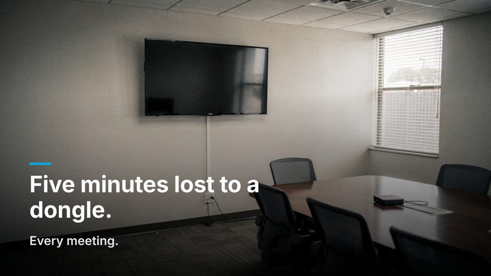 Empty conference room with wall-mounted display, cable to a floor box, and a dongle left on the table.
