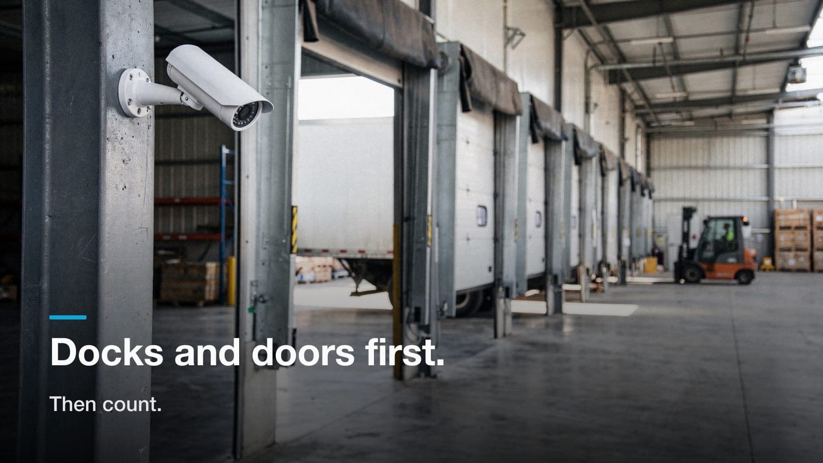 Bullet camera on a warehouse column aimed down a row of dock doors with a trailer backed into one bay.