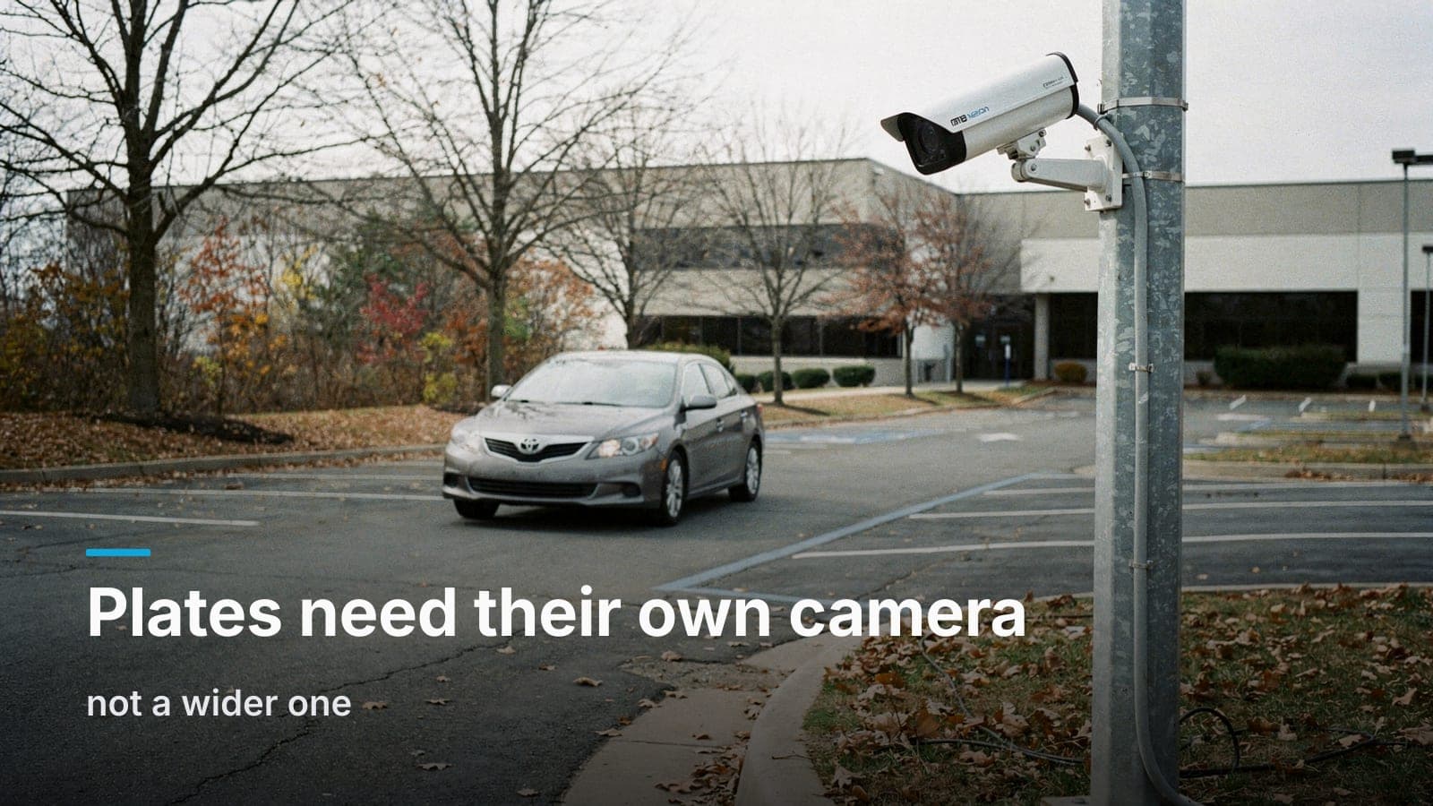 Bullet camera on a short pole aimed low down a single-lane parking lot entrance as a sedan pulls in.