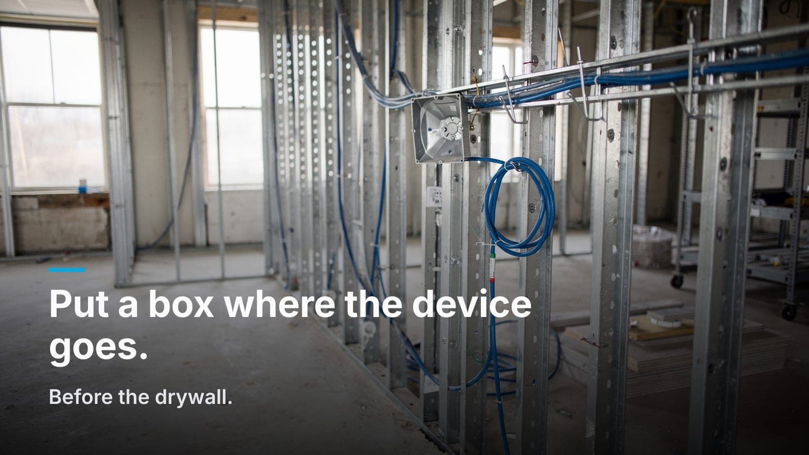 Blue Cat6 cable through metal studs with a blank low-voltage back box and service loop on a J-hook.