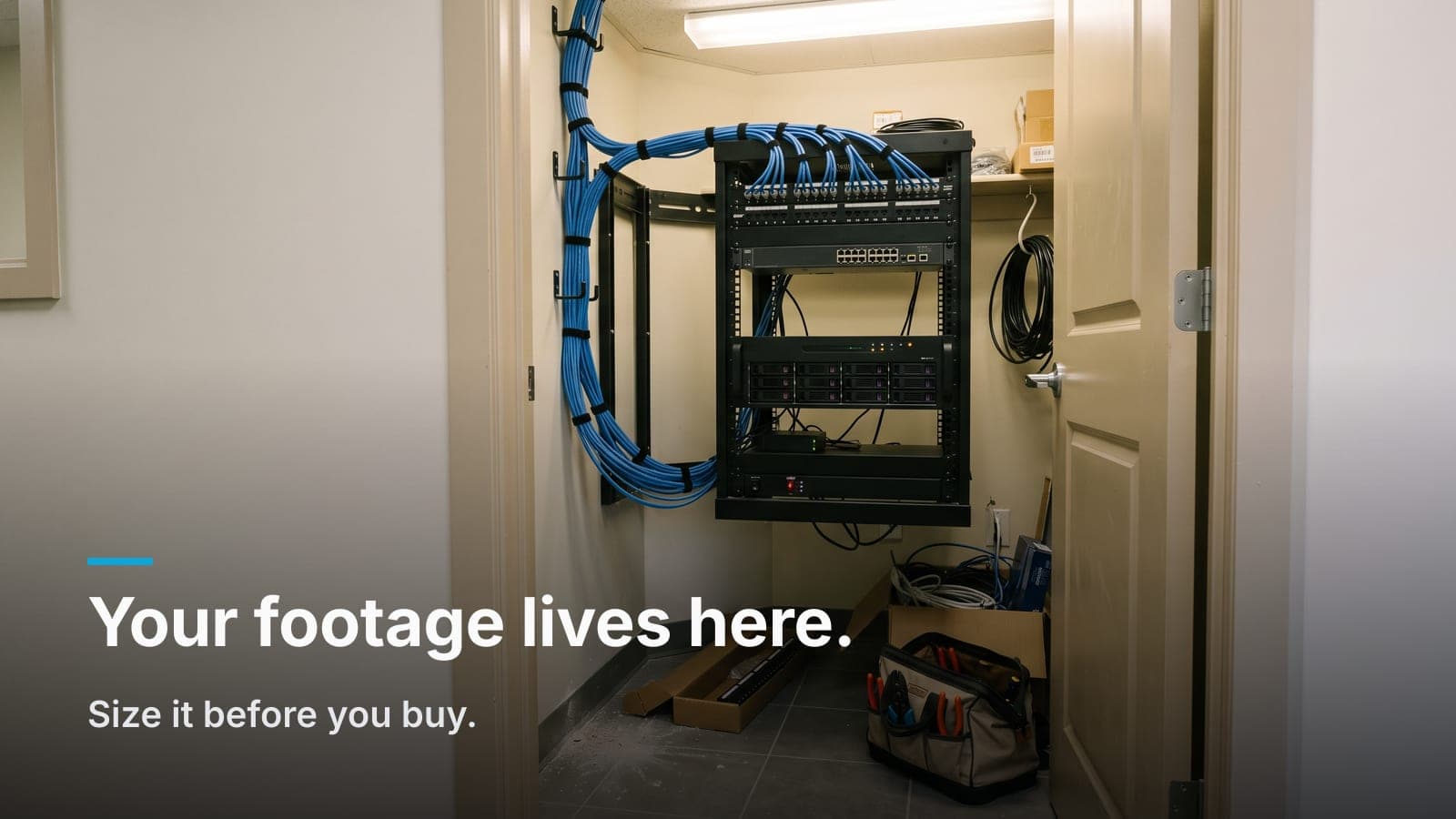 Wall-mounted rack in an office closet with a camera recorder, patch panel, and blue cable bundle.