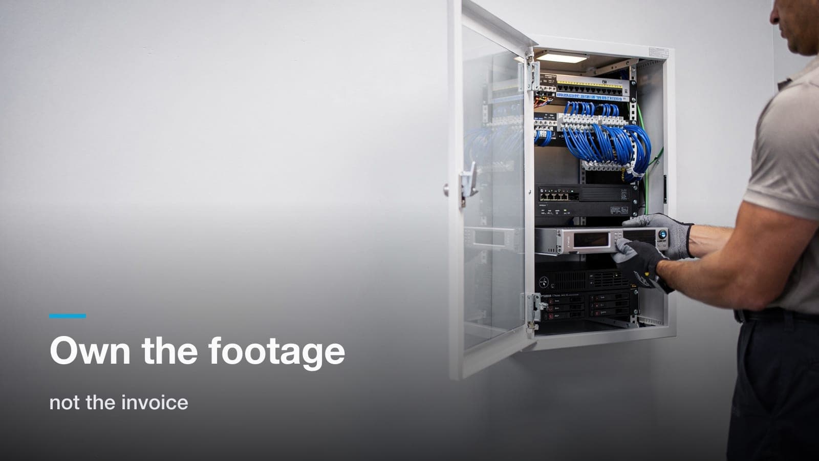Technician sliding a hard drive tray into a network video recorder in a wall-mounted office rack.