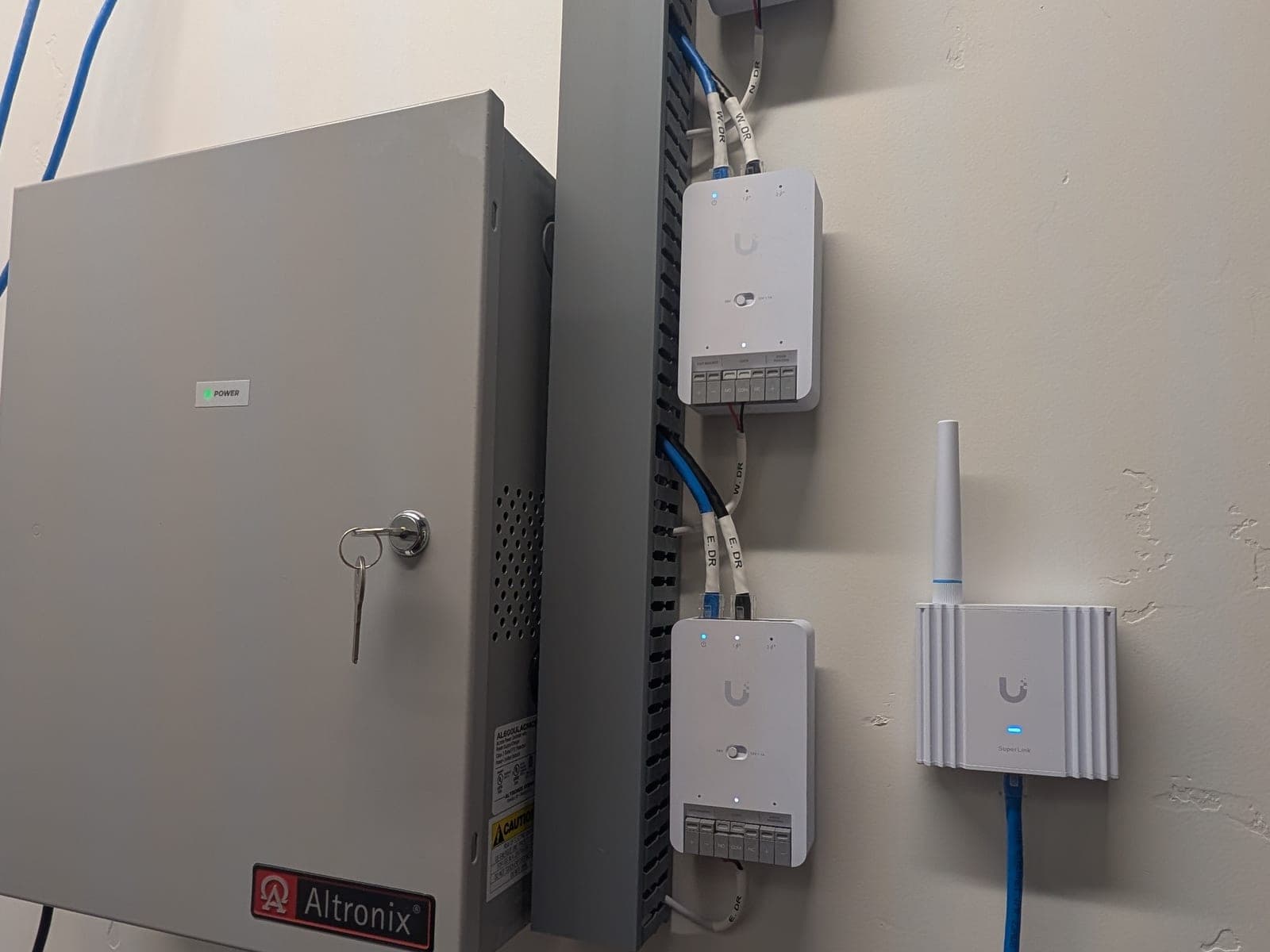 Altronix power cabinet next to three UniFi Access hubs on a wire cable tray and a wireless access point