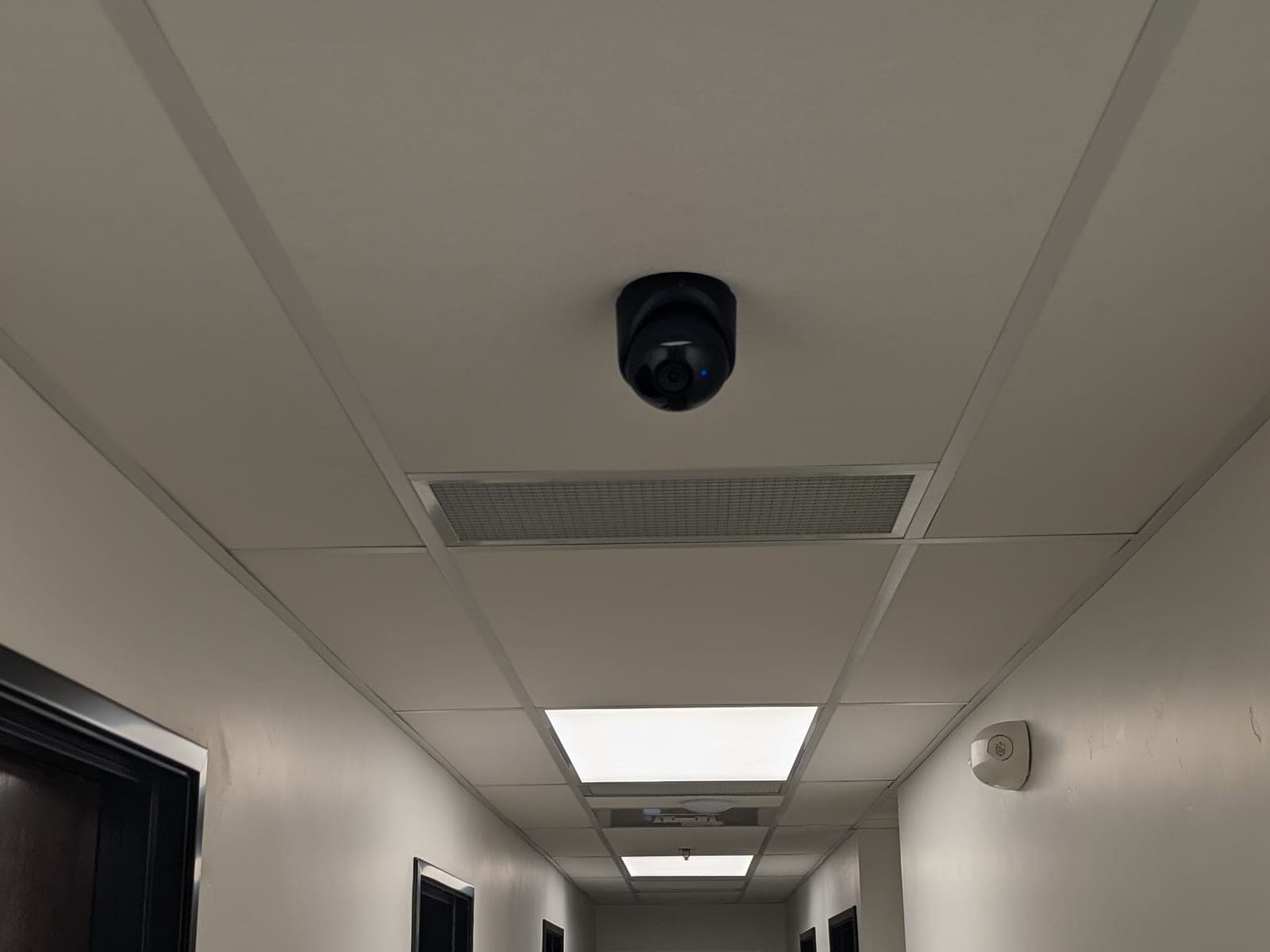 Black dome security camera mounted flush in a drop ceiling above an office hallway